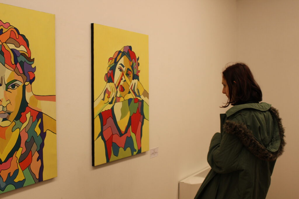 Person looks at figurative painting of someone making a triangle shape with hands