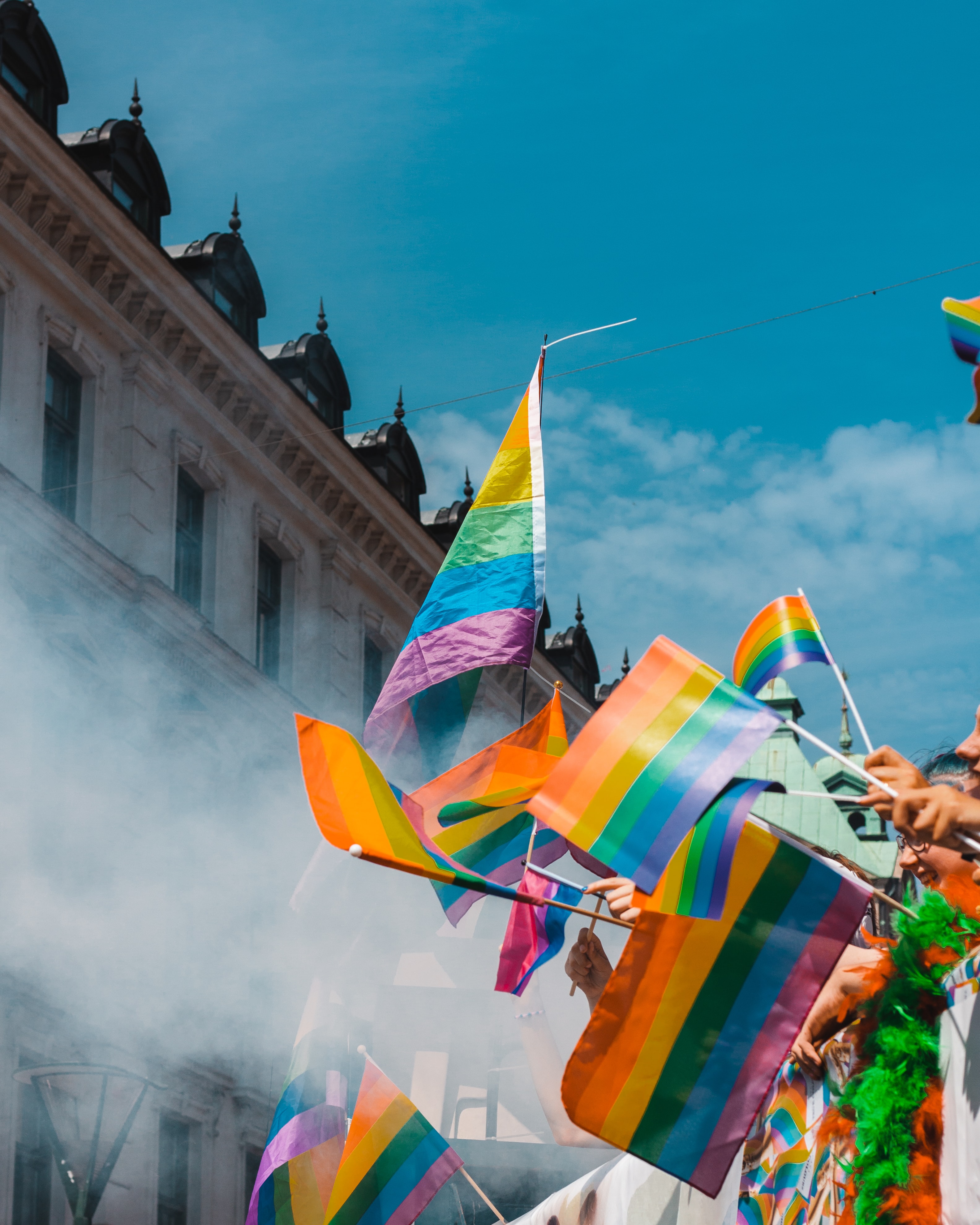 Hands waving rainbow flags against a skyline and sky